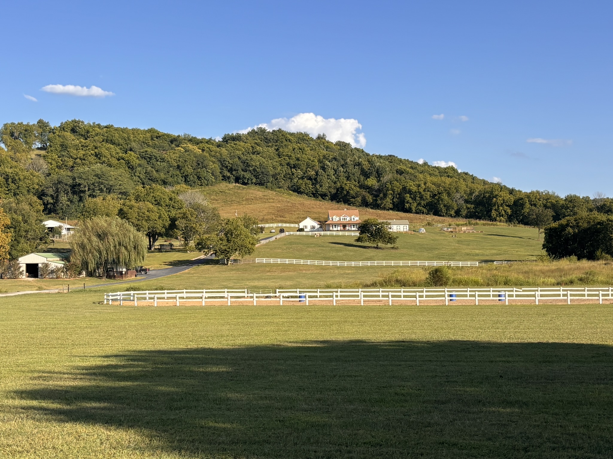 Wide view of the farmhouse, paddocks, and white fencing on a clear day